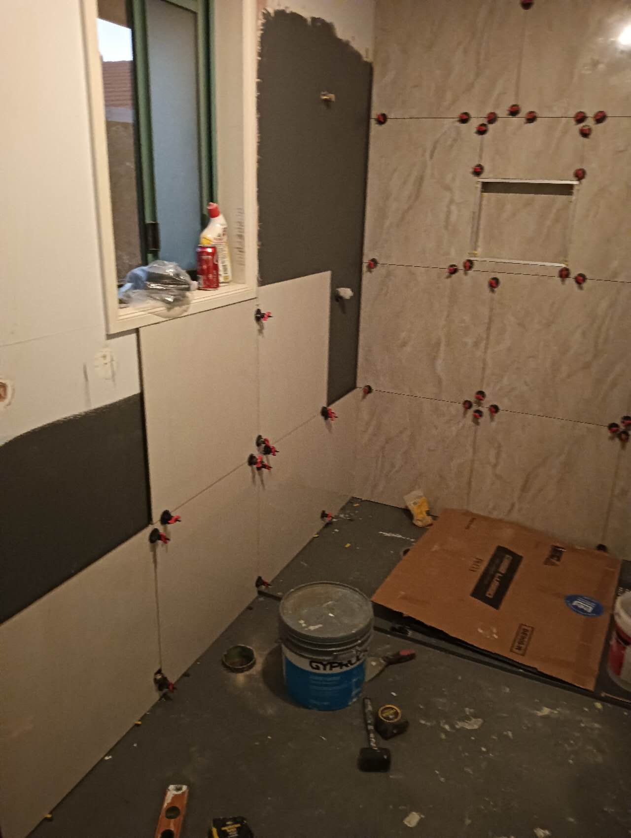 Large grey bathroom tiles being installed around a shower recess and window
