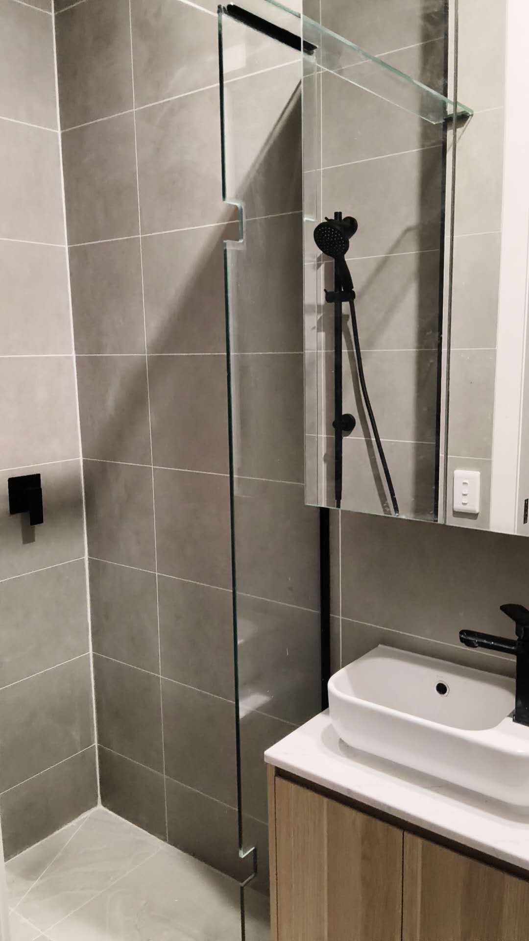 Completed grey tiled bathroom with black-framed shower screen and timber vanity